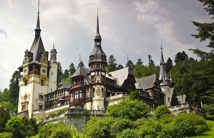 Peleș Castle in Romania with lush green forest and dramatic cloudy sky