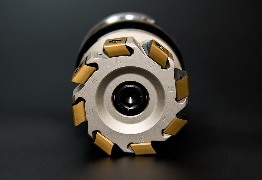 Close-up of CNC milling cutter with gold carbide inserts on dark background