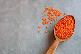 Red lentils in wooden spoon on gray background