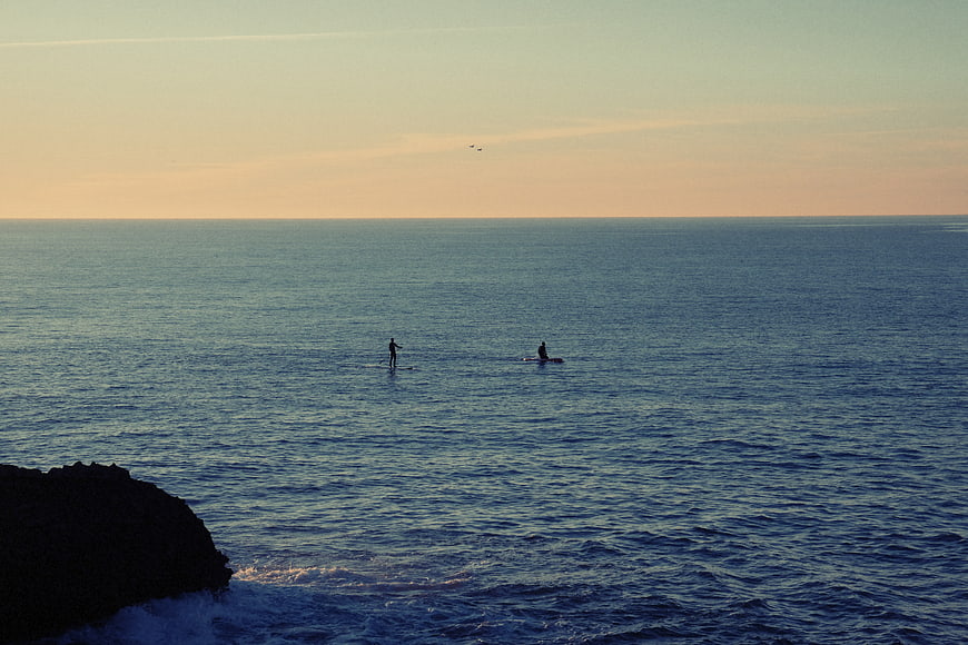 Two paddle boarders on calm ocean at sunset