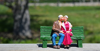 Miniature elderly couple figurine kissing on green bench