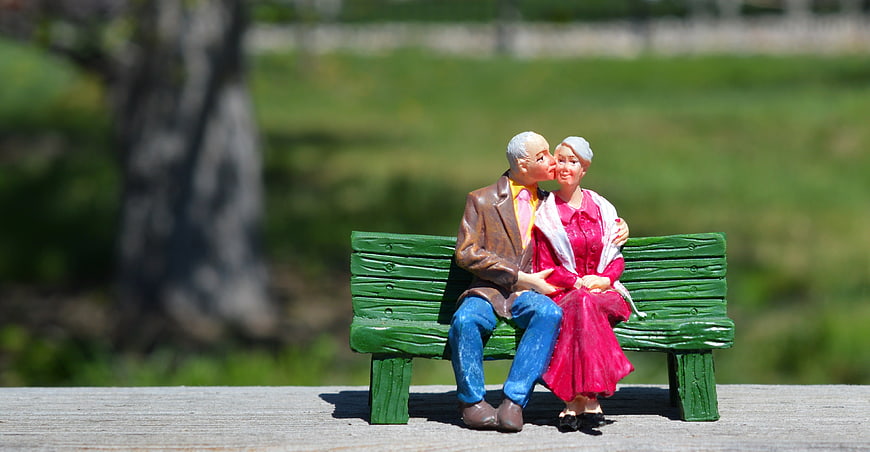 Miniature elderly couple figurine kissing on green bench