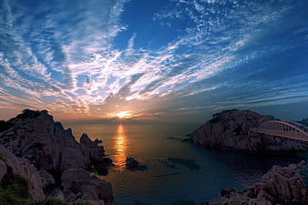 Sunrise over rocky coastal cliffs with bridge and ocean reflection