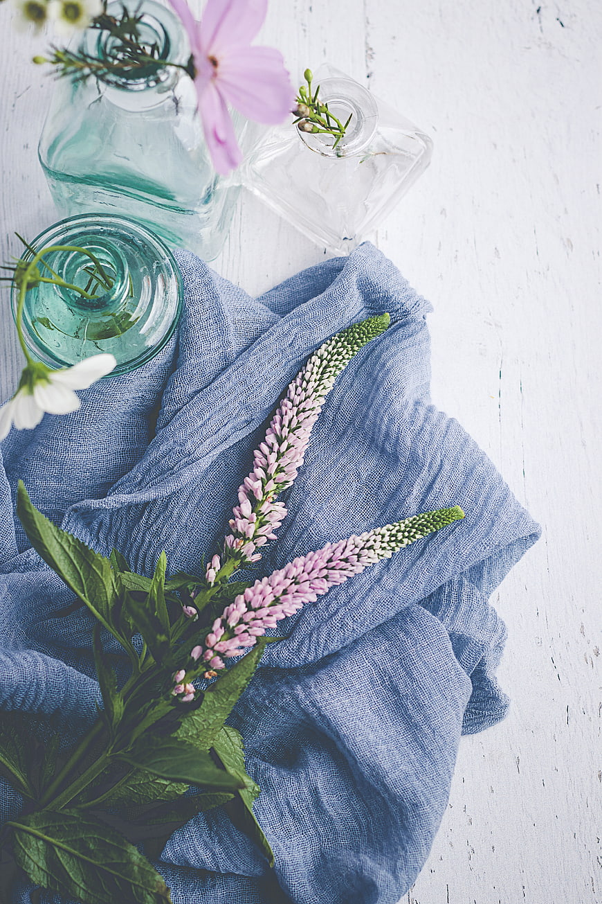 Flat lay of pink flowers and blue linen on white wood