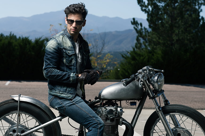 Man in denim jacket sitting on custom motorcycle outdoors