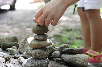 Child's hand balancing smooth river stones into a vertical tower