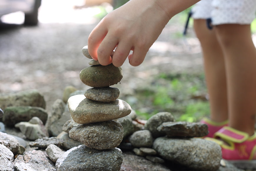Child's hand balancing smooth river stones into a vertical tower