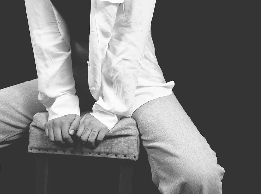 Black and white photo of woman sitting on stool with hands