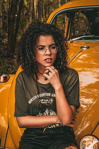 Woman with curly hair leaning on vintage yellow car