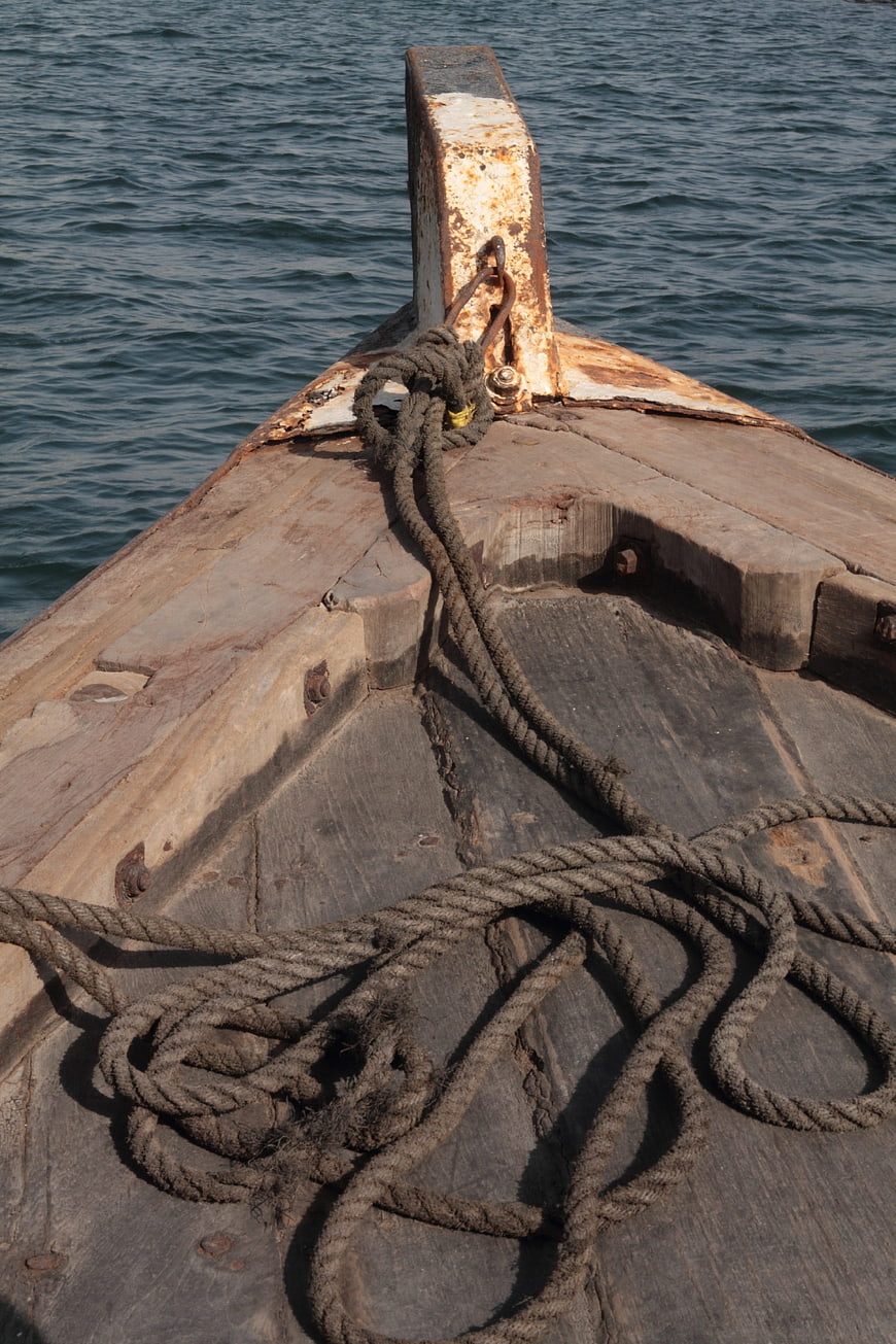 Close-up of weathered wooden boat bow with rope on sea