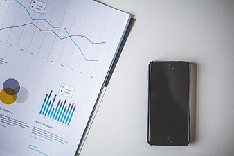 Black smartphone next to business report with charts