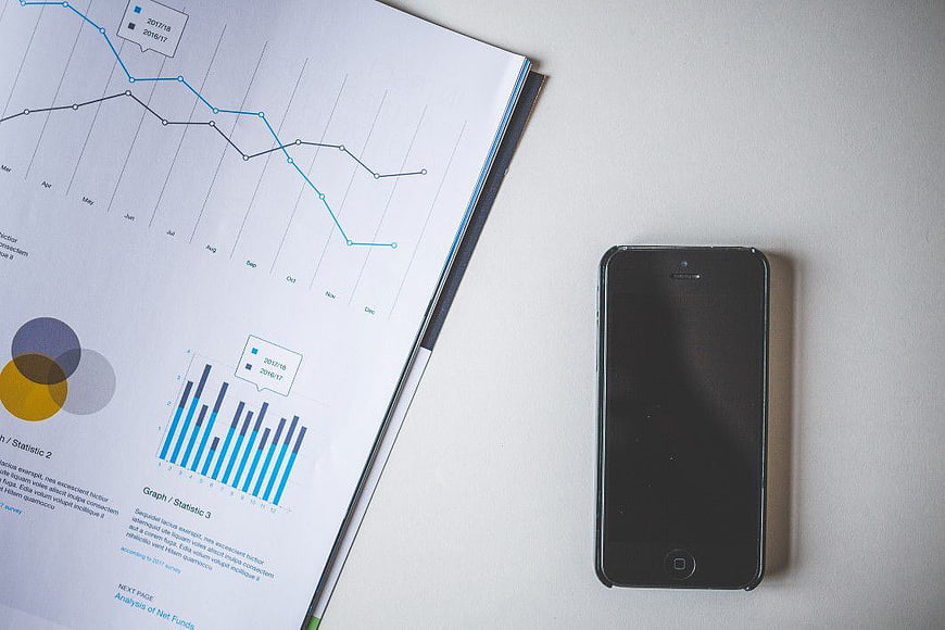Black smartphone next to business report with charts