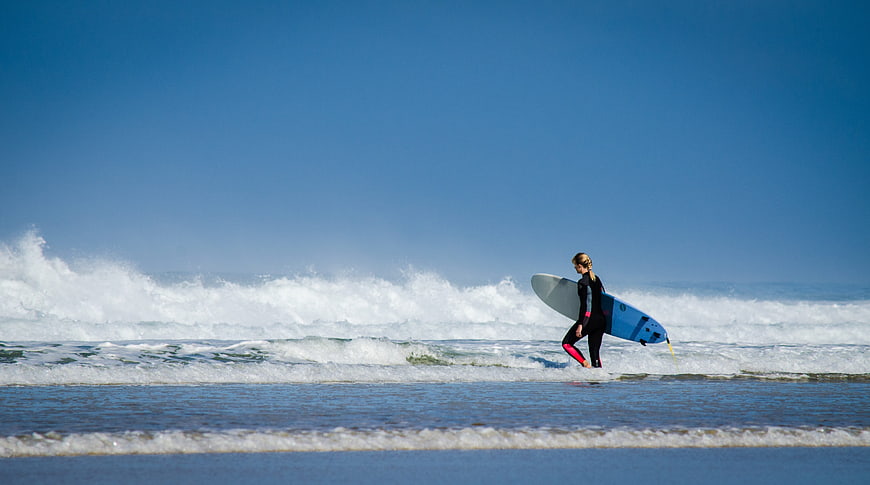 Woman walking on beach with surfboard