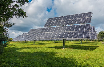 Solar panels in a green field under a cloudy sky