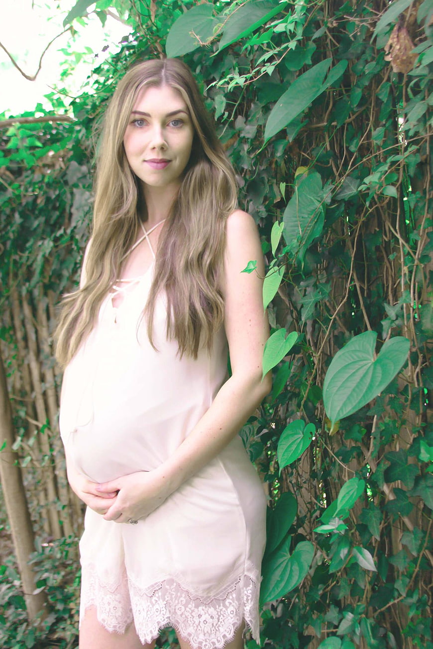 Pregnant woman in white dress holding belly outdoors