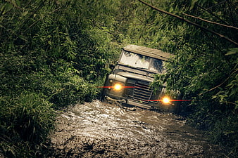 Vintage off-road vehicle driving through muddy forest trail