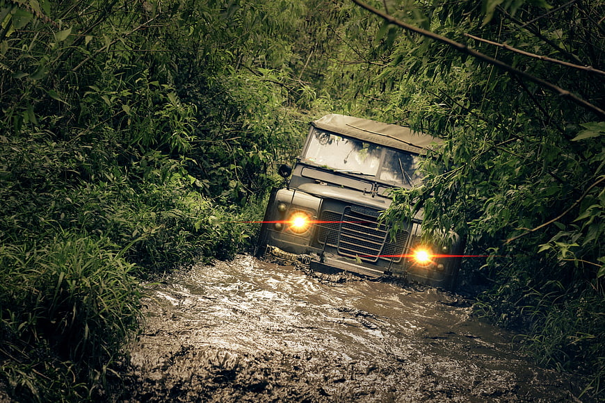 Vintage off-road vehicle driving through muddy forest trail