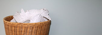 Woven Wastebasket Filled With Crumpled White Paper Against Gray Wall