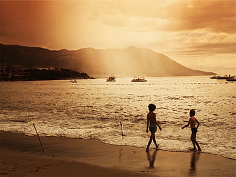 Two boys playing on beach at sunset with mountains