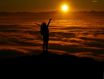 Silhouette of Hiker Celebrating on Mountain Peak Above Clouds at Sunset
