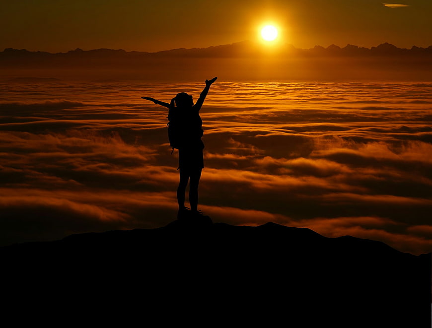 Silhouette of Hiker Celebrating on Mountain Peak Above Clouds at Sunset