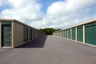 Empty outdoor self-storage facility aisle with green roll-up doors