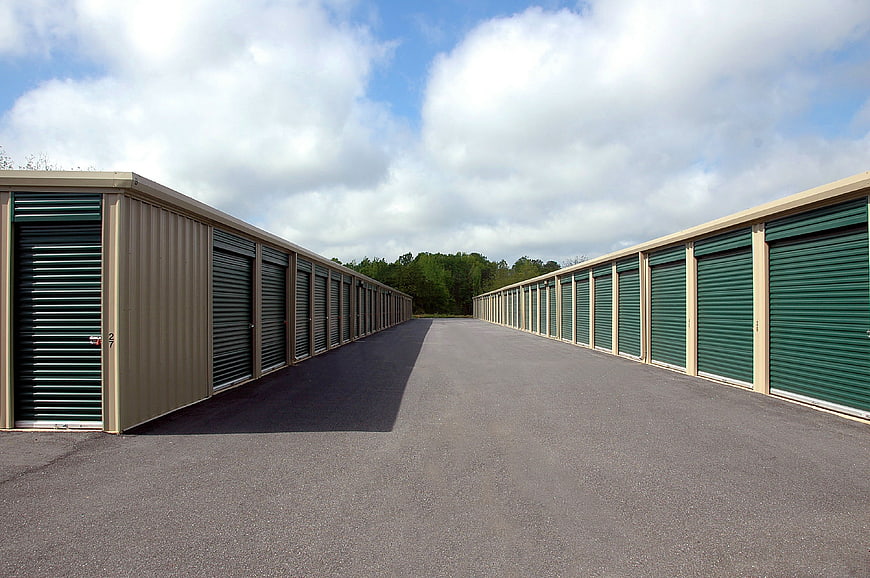 Empty outdoor self-storage facility aisle with green roll-up doors