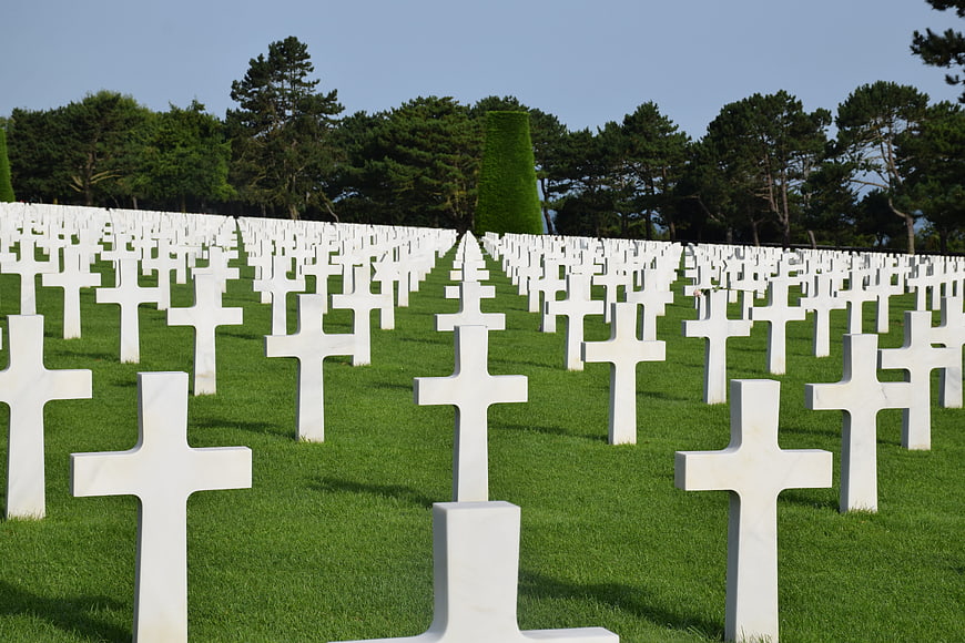 Rows of white crosses in a military cemetery with green lawn and trees