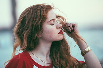 Redhead woman with red lipstick touching hair by water