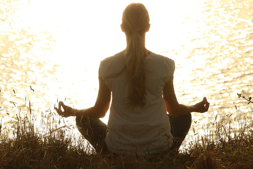 Woman Meditating by Lake at Sunset