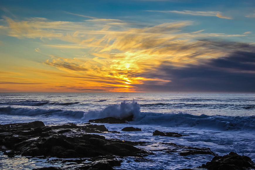 Dramatic Sunset Over Rocky Ocean Coast with Crashing Waves