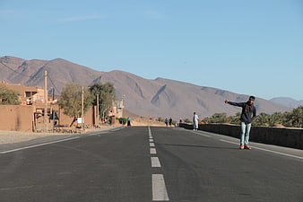 Man hitchhiking on desert road with mountains background