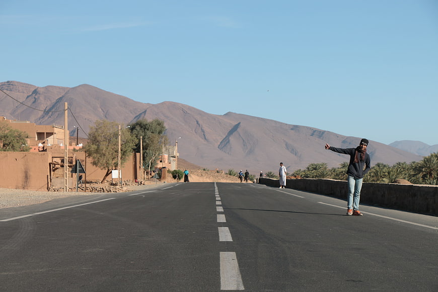 Man hitchhiking on desert road with mountains background