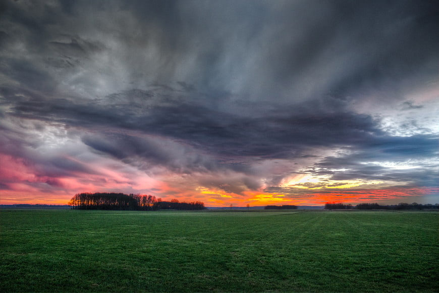 Dramatic sunset over green field with storm clouds