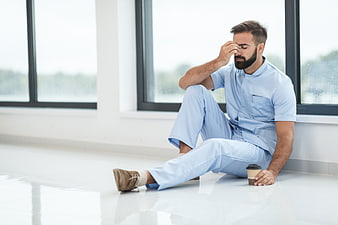 Exhausted male nurse sitting on hospital floor with coffee