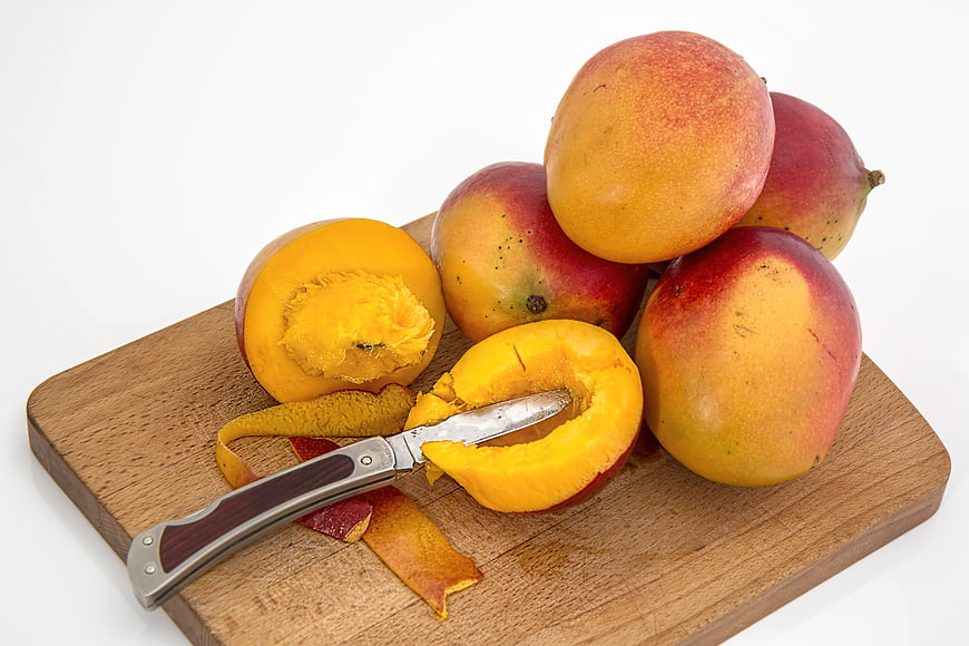 Fresh ripe mangoes on wooden cutting board with knife
