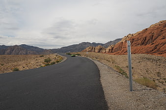 Green sports car driving on winding desert highway near red rock canyon