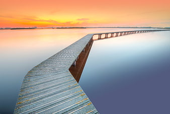 Long wooden pier extending into calm water at sunset