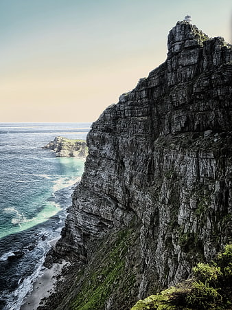 Dramatic coastal cliff with lighthouse and turquoise ocean