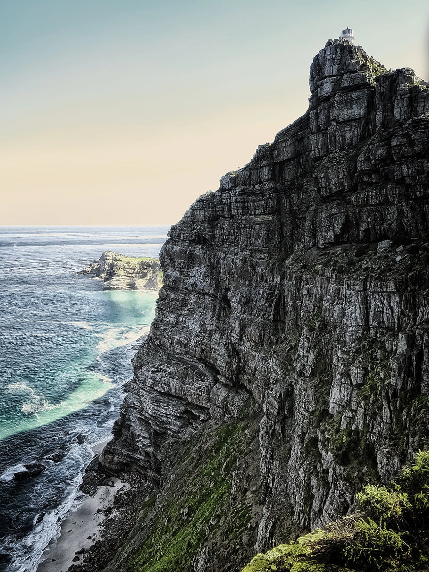Dramatic coastal cliff with lighthouse and turquoise ocean