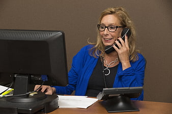 Professional woman talking on phone at office desk with computer monitor