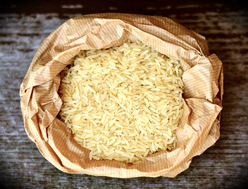 Uncooked rice grains in a brown paper bag on wood