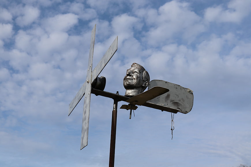 Metal windmill with sculpted head against cloudy blue sky