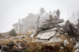Man standing on rocky mountain peak in foggy weather