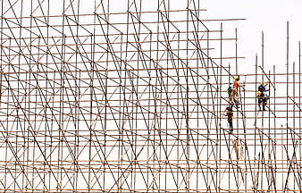 Construction Workers Climbing Rusty Metal Scaffolding Against White Sky