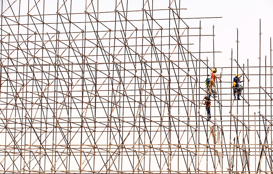 Construction Workers Climbing Rusty Metal Scaffolding Against White Sky