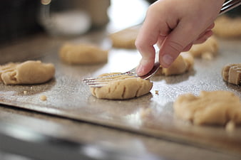 Hands Using Fork To Press Pattern Into Raw Cookie Dough On Baking Sheet