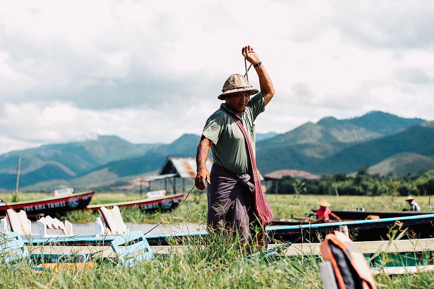 Man pulling boat rope in grassy field with mountains