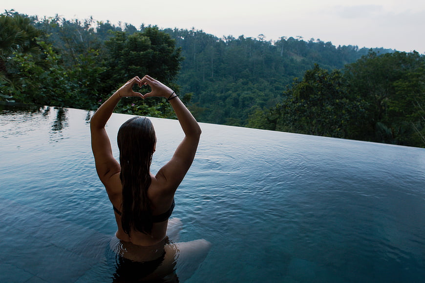 Woman making heart shape in infinity pool overlooking jungle
