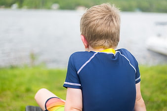 Back view of young boy sitting by lake in summer